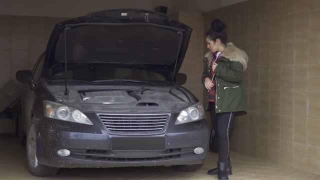 Young woman tries to repair the car engine with wrench