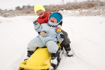 Two brother's boys are having fun riding a new yellow sled. Children, best friends are happy on a winter day. Active rest with children. Casual boy's fashion