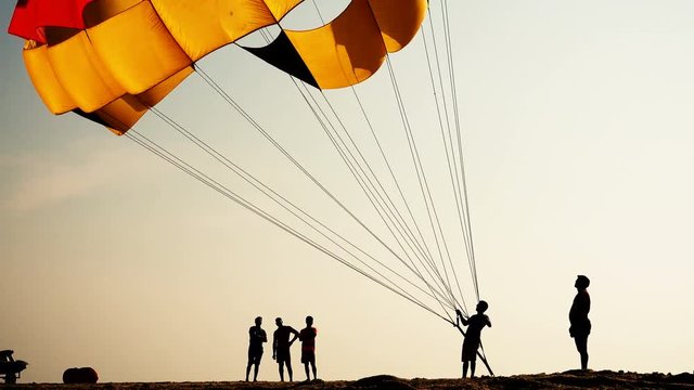 Silhouettes of people on the beach. They inflate and lift the parachute into the air.