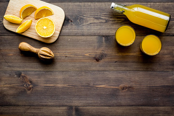 Healthy vitamin drink. Fresh orange juice near fruits and juicer on dark wooden background top view copyspace