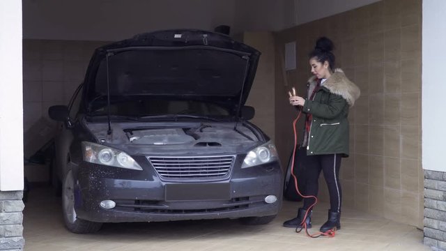 Beautiful woman with jumper cables in garage
