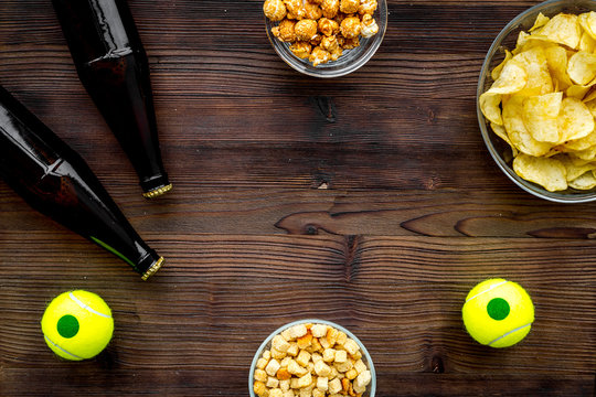 Snacks for watching sport matches and games on TV. Crisps, popcorn, rusks near drink and ball on dark wooden background top view copyspace