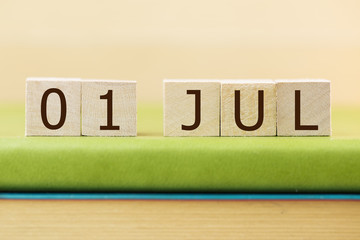 Wooden cube shape calendar for JUL 1 on green book, table. 
