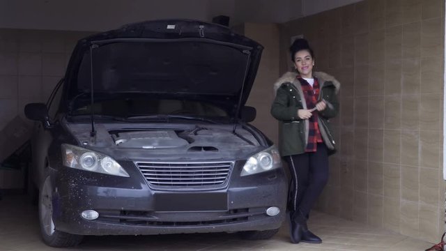 Beautiful woman posing near car in garage with wrench in hand