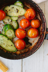Roasted cherry tomatoes and cucumbers in black frying pan.