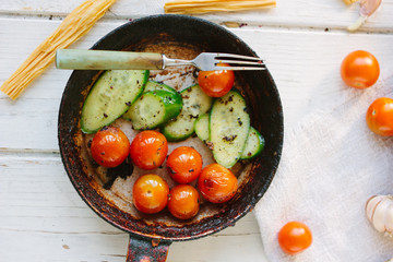 Roasted cherry tomatoes and cucumbers in black frying pan.