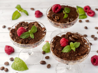Dessert Tiramisu in glass goblet with mint coffee beans and fresh raspberries on white wooden table