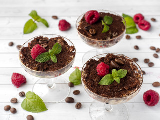 Dessert Tiramisu in glass goblet with mint coffee beans and fresh raspberries on white wooden table