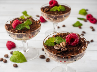 Dessert Tiramisu in glass goblet with mint coffee beans and fresh raspberries on white wooden table