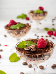 Dessert Tiramisu in glass goblet with mint coffee beans and fresh raspberries on white wooden table