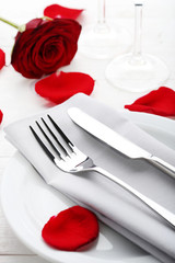 Fototapeta na wymiar Kitchen cutlery in white plate with red rose petals on wooden table
