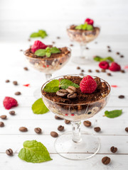 Dessert Tiramisu in glass goblet with mint coffee beans and fresh raspberries on white wooden table