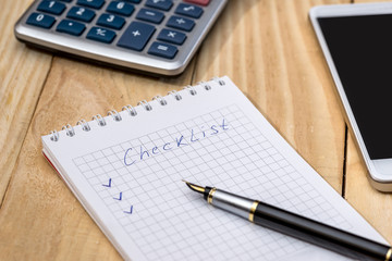 checklist on a notepad with pen and calculator on desk