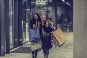 Two cute young adolescent women, heavy loaded with christmas gifts,  shopping, while walking along store windows and choosing and admiring the items. 