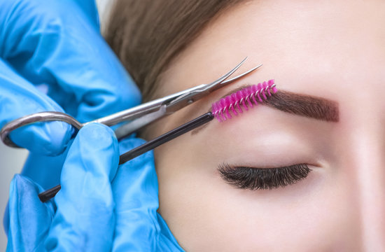 The make-up artist cuts her eyebrows with scissors. A girl with beautiful long eyelashes and well-groomed eyebrows.