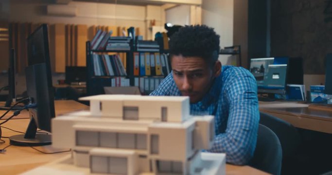 Young confident African American black male architect working on a private house project in the office, studying mansion model. 4K UHD