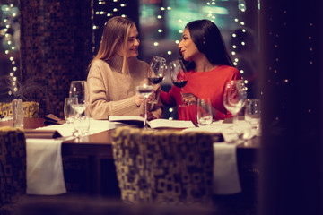 Two adolescent women going through the menue  in a fancy restaurant, while drinking a glass of red wine and laughing and talking, maybe gossiping