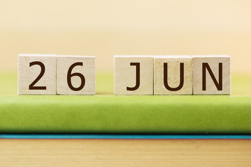 Wooden cube shape calendar for JAN 26 on green book, table.