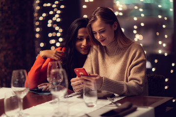 Two adolescent women going through the menue  in a fancy restaurant, while drinking a glass of red wine and laughing and talking, maybe gossiping