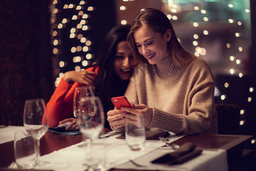 Two adolescent women going through the menue  in a fancy restaurant, while drinking a glass of red wine and laughing and talking, maybe gossiping