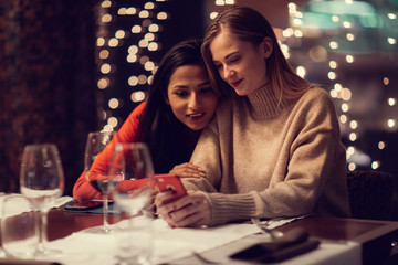 Two adolescent women going through the menue  in a fancy restaurant, while drinking a glass of red wine and laughing and talking, maybe gossiping