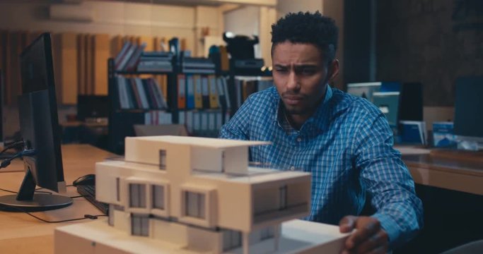 Young confident African American black male architect working on a private house project in the office, studying mansion model. 4K UHD