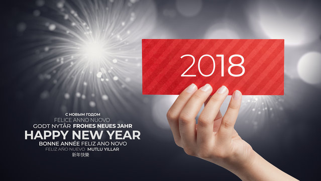 female hand holding new year greeting card in different languages on background with fireworks and bokeh lights