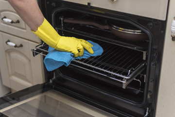 Women's hand in protective gloves wipes the kitchen gas stove with a blue rag.