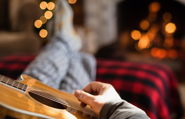 Closeup of man's hand strumming guitar with feet up in front of a cozy fire