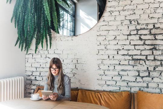 Pretty Caucasian woman sitting at cafe and reading on tablet.