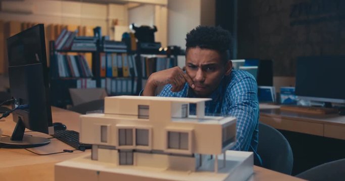 Young confident African American black male architect working on a private house project in the office, studying mansion model. 4K UHD