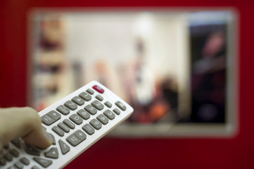 The remote in the hand switch channels on the TV hanging on the red wall