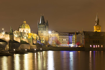 Fototapeta na wymiar Night snowy Prague Old Town with Bridge Tower and St. Francis of Assisi Cathedral and Charles Bridge with its baroque Statues, Czech republic