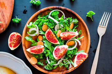 Autumn salad of arugula, figs in a brown earthenware plate on a dark background. top view