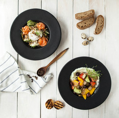 Salad with fresh salmon, grilled zucchini and poached eggs and a plate of hummus and vegetables on a white wooden table