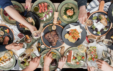 beautifully served table with different restaurant dishes and hands with glasses of wine