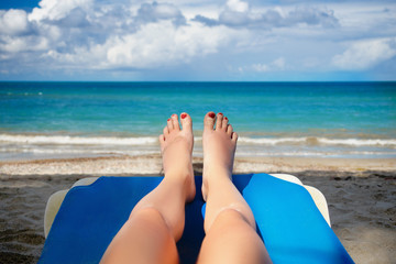 female legs and feets with red nails on sunbed on the beach