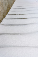 Fresh snowfall covering up a set of outdoor concrete stairs
