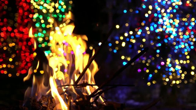 Fire burning with Christmas light bokeh in the background during the holidays.