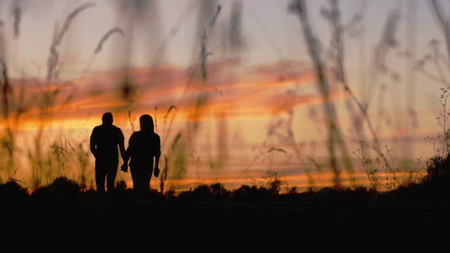 Silhouette of walking couple. Man and woman go hand in hand outdoors on a sunset sky background.