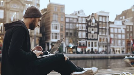 4K Young creative businessman uses laptop outside. Successful man working near beautiful river embankment, old town. - Powered by Adobe