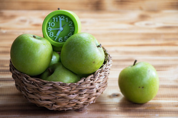 Closeup group of green apple and clock in woven basket put beside blurred green apple on wooden timber board,blurry background