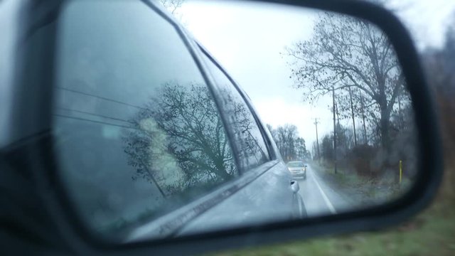 Rear view mirror image of car following distance through dangerous rainy road