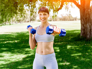 Portrait of cheerful woman in fitness wear exercising with dumbbell