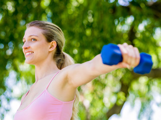 Portrait of cheerful woman in fitness wear exercising with dumbbell