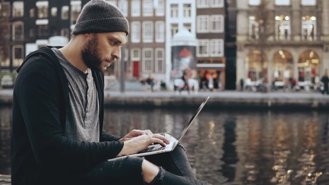 4K Young man working in mobile office outside. Creative worker in beautiful old town scenery. Amazing water reflection.