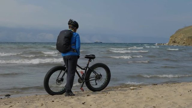 Fat bike also called fatbike or fat-tire bike in summer driving on the beach. The guy walks along the beach and leads a bicycle next to him. He rests from the trip and enjoys the view of the sea.