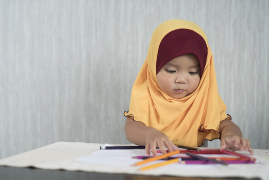 asian little toddler / baby girl wearing hijab is having fun learning to use pencils. Education concept. human growth concept.