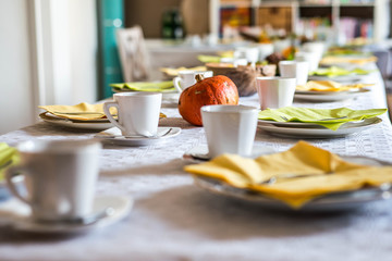 Beautiful festive dinner table colorful yellow fall helloween pumpkin decoration coffee mugs saucers plates and spoons