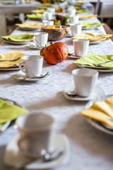 Beautiful festive dinner table colorful yellow fall helloween pumpkin decoration coffee mugs saucers plates and spoons